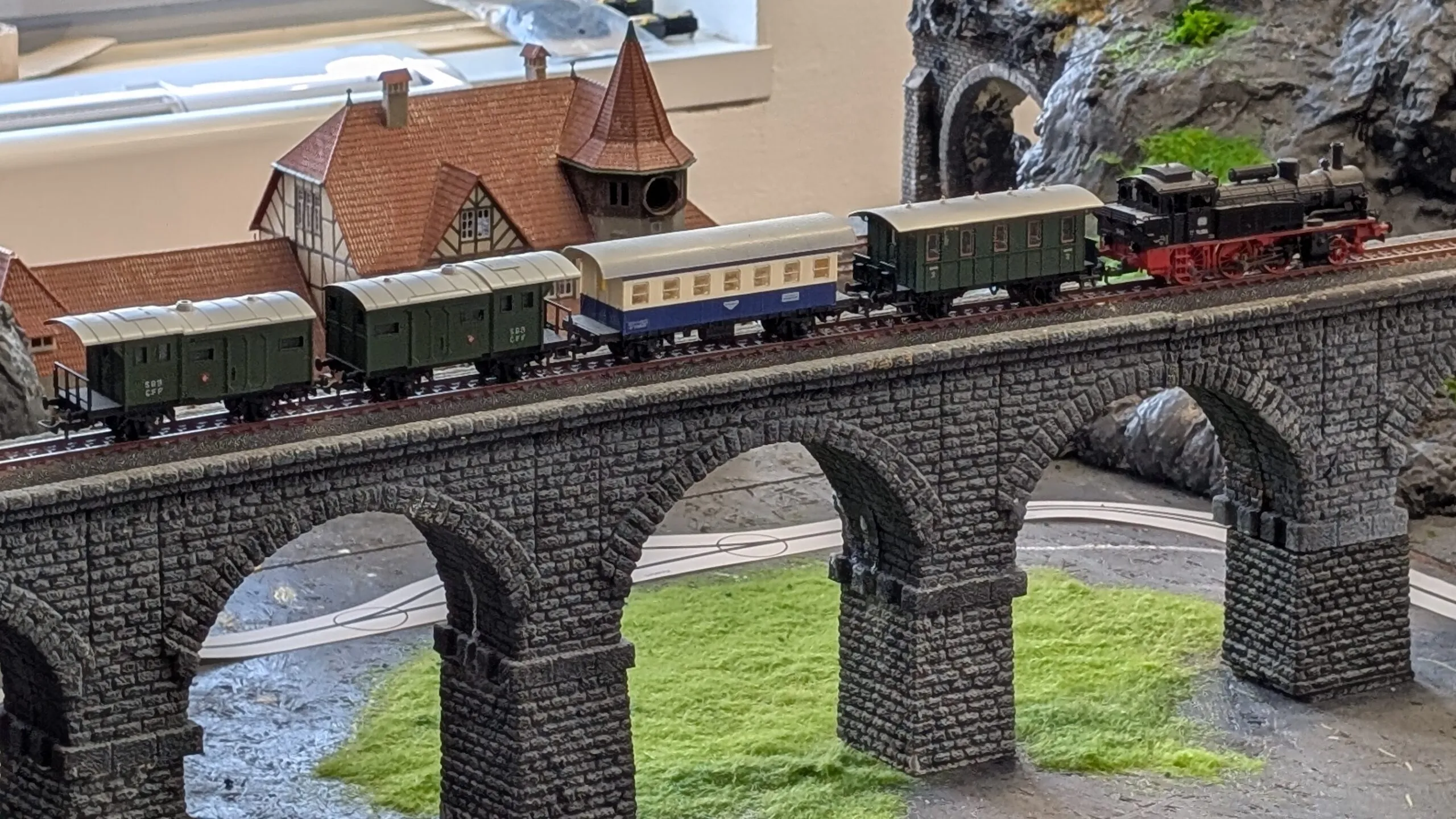 Der Zug mit seinen Waggons rollt majestätisch über die Viaduktbrücke. Unter ihm windet sich die neue Straße hinunter zum kleinen Bahnhof im Tal