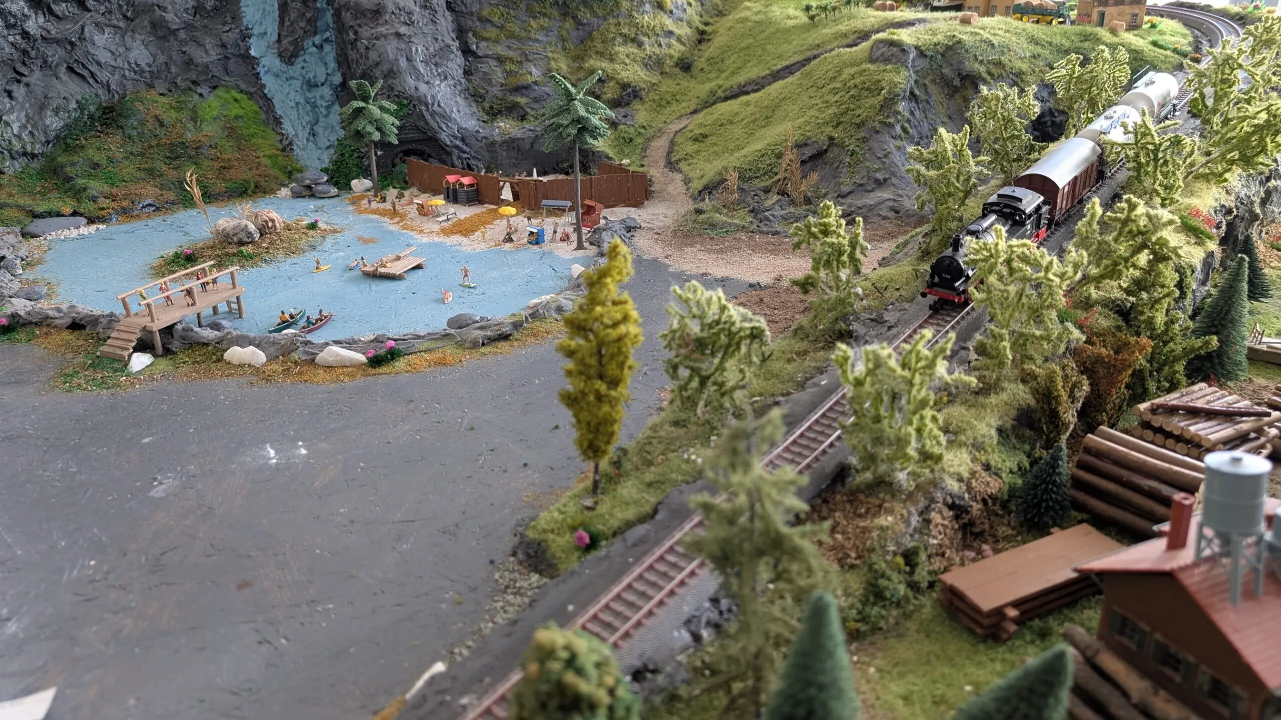 Die Lok mit ihren Waggons rauscht von Berg zu Tal und fährt dabei am Badesee und dem Sägewerk vorbei